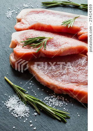 Raw pork steaks with rosemary on black stone Raw pork steaks with rosemary on black stone 25414369