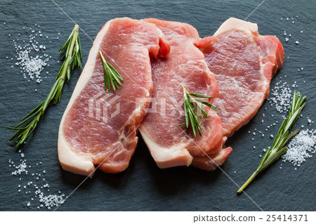 Raw pork steaks with rosemary on black stone Raw pork steaks with rosemary on black stone 25414371