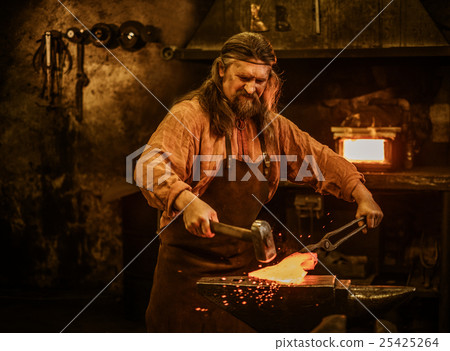 Senior blacksmith forging the molten metal on the Senior blacksmith forging the molten metal on the 25425264