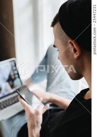 Rear view of man using cellphone and laptop Rear view of man using cellphone and laptop 25447231