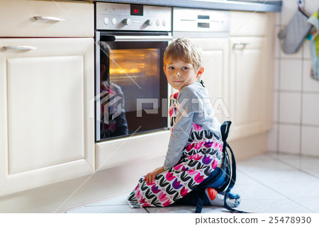 Funny blond kid boy baking muffins indoors 25478930