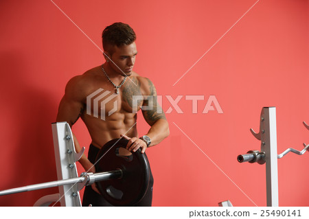 At gym. Image of bodybuilder standing near barbell At gym. Image of bodybuilder standing near barbell 25490141