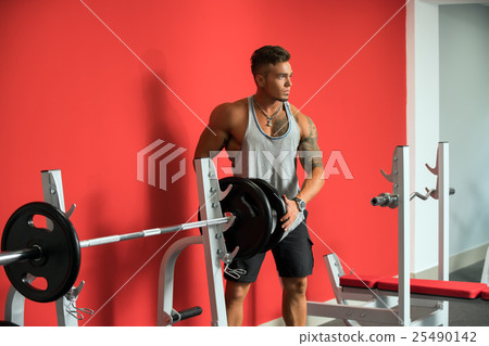 Tattooed young athlete standing near barbell Tattooed young athlete standing near barbell 25490142