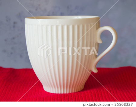 White mug stands on a red scarf, blurred blue White mug stands on a red scarf, blurred blue 25508327