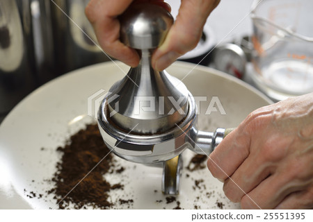Barista using a tamper to press ground coffee 25551395
