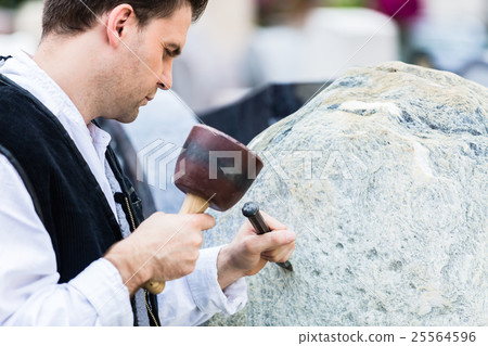 Sculptor with mallet working on erratic block 25564596