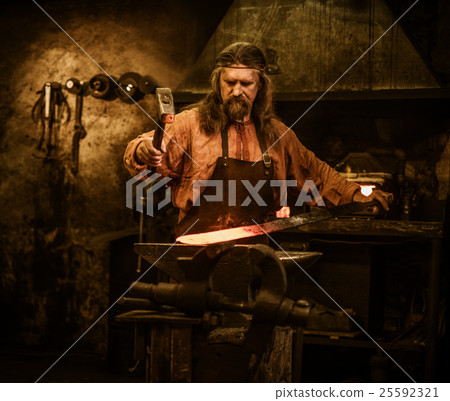 Senior blacksmith forging the molten metal on the Senior blacksmith forging the molten metal on the 25592321