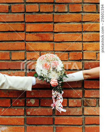 Two hands holding wedding bouquet against brick wall. 25601394