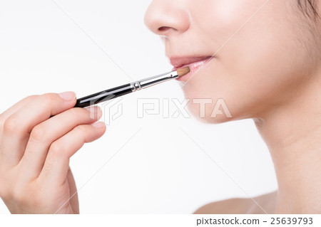 A woman applying a lipstick with a brush A woman applying a lipstick with a brush 25639793