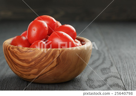 red cherry plum tomatoes in olive bowl on wood table 25640798