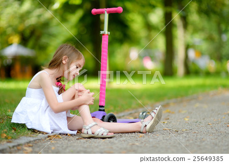 Little girl sitting on the ground after she fell while riding her scooter 25649385