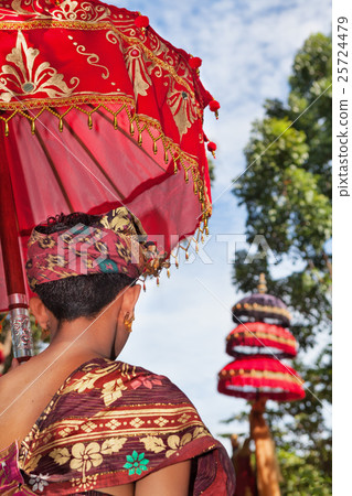 Balinese man in sarong hold umbrella in temple 25724479