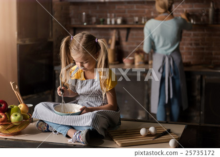 Involved girl mixing eggs sitting on the table 25735172
