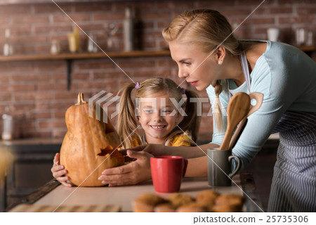 Delighted girl touching a pumpkin with her mother 25735306