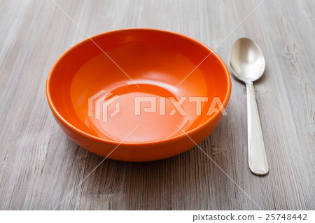 orange bowl with steel spoon on gray brown table 25748442