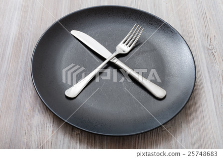 black plate with crossing knife, spoon on gray black plate with crossing knife, spoon on gray 25748683
