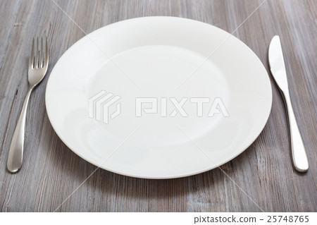 white plate, knife, spoon on gray brown table 25748765