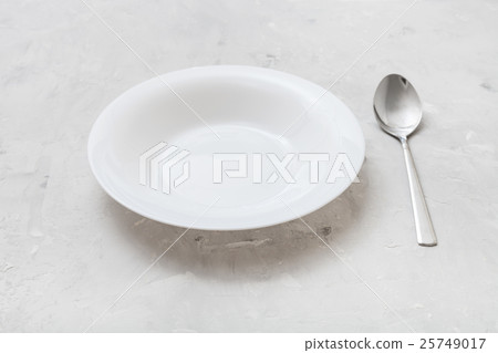 white deep plate and metal spoon on gray concrete white deep plate and metal spoon on gray concrete 25749017