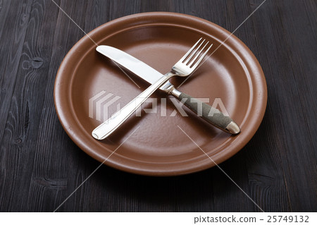 brown plate with crossing knife, spoon on dark brown plate with crossing knife, spoon on dark 25749132