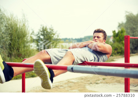 young man doing sit up on parallel bars outdoors 25788310