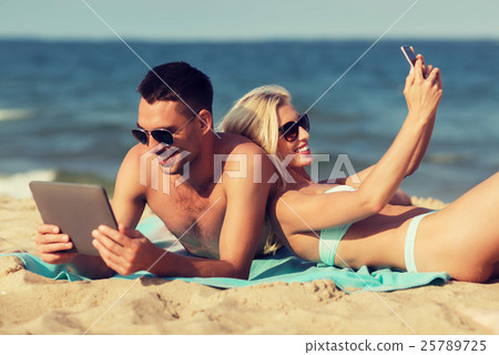 happy couple with modern gadgets lying on beach 25789725