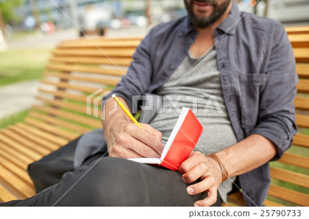 close up of man writing to notebook on city street 25790733