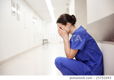 Stock Photo: sad or crying female nurse at hospital corridor