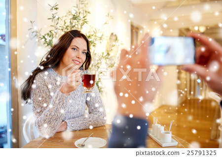 man taking picture of woman by smartphone at cafe 25791325