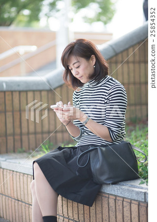接觸智能手機的中間女性戶外 接觸智能手機的中間女性戶外 25854352