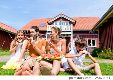 Family sitting in grass front of home and eating Family sitting in grass front of home and eating 25870951