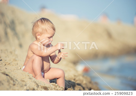 Cute baby playing with toys on sandy beach near 25909823