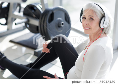 Pretty senior woman using headphones in a gym. 25932389