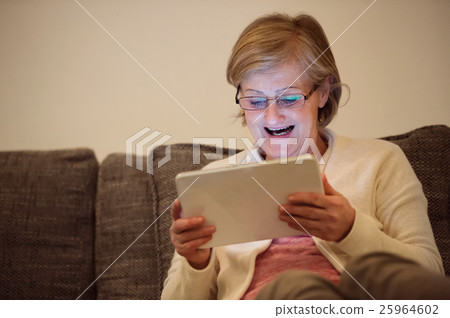 Senior woman with tablet sitting on couch in Senior woman with tablet sitting on couch in 25964602