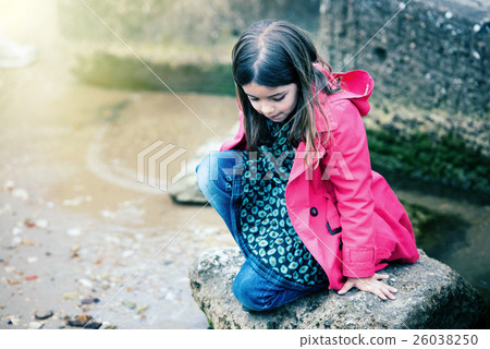 pretty little girl playing on a rock at the water's edge 26038250