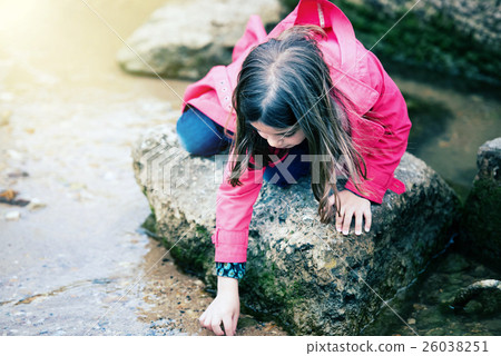 pretty little girl playing on a rock at the water's edge 26038251