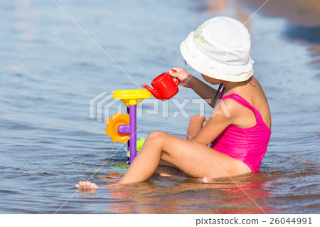 Five-year girl in a pink bathing suit sitting in on the river bank and plays in the sand toys 26044991