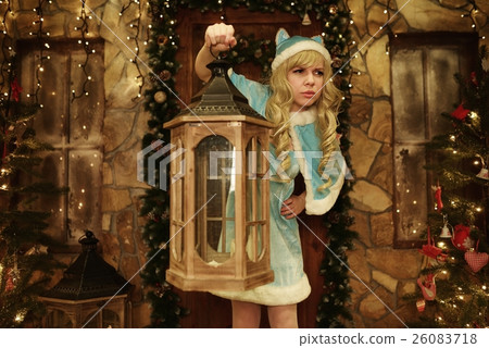 Snow Maiden holds lantern on doorstep of house decorated in Christmas style 26083718