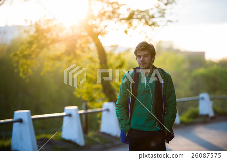Common young man walking in the city listening to Common young man walking in the city listening to 26087575