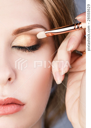 Artist applying eyeshadow on model's eye. 26088629
