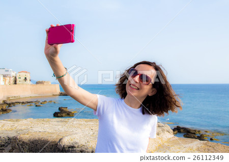 young woman takes selfie in front to the sea with a smartphone 26112349