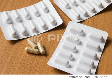 Brown capsule with white blister on wooden table 26133540