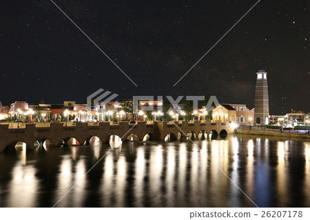 Scenery of the river bridge into the village at night with bright lights. 26207178
