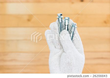 Hand in glove holding metal anchor bolts Hand in glove holding metal anchor bolts 26208843