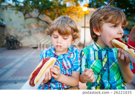 Two little kid boys eating hot dogs outdoors Two little kid boys eating hot dogs outdoors 26221835
