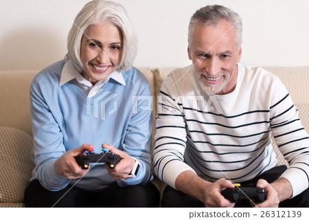 Delighted aged couple playing with game console at Delighted aged couple playing with game console at 26312139