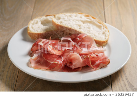 speck slices on white plate with ciabatta on old 26329437