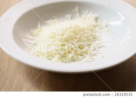 grated parmigiano in white plate over wood table 26329535