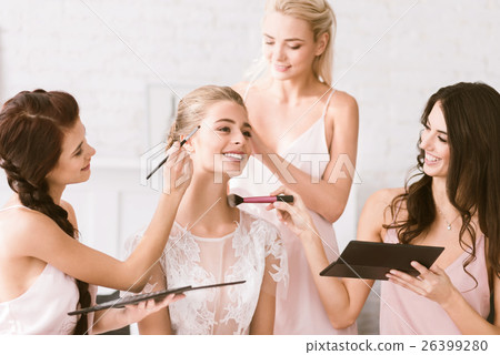 Cheerful bridesmaids helping the bride to get 26399280