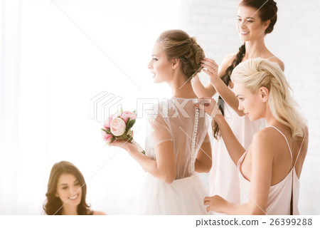 Delighted bridesmaids helping the bride to get 26399288