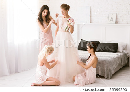 Delighted bridesmaids helping the bride to get 26399290